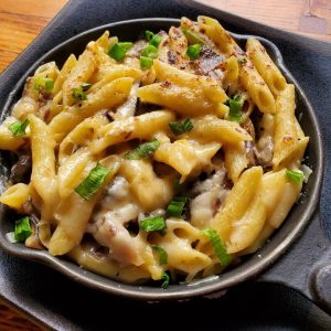 Cheesy pasta with mushrooms and green onions in a skillet.