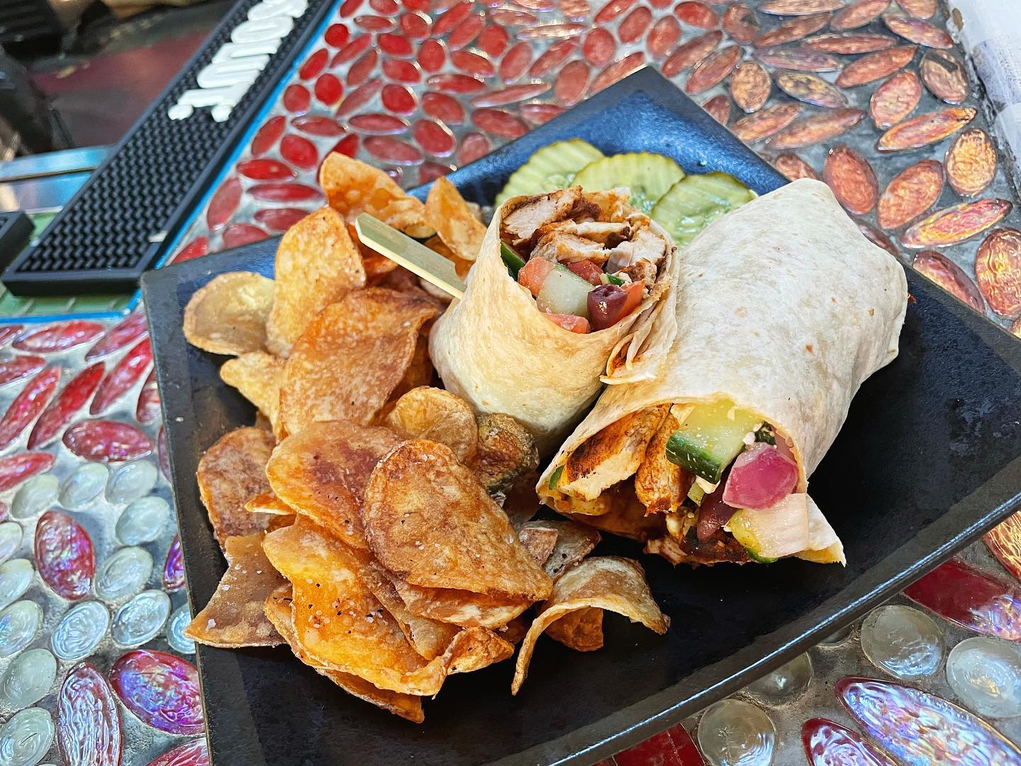 A black plate with chips and a burrito.